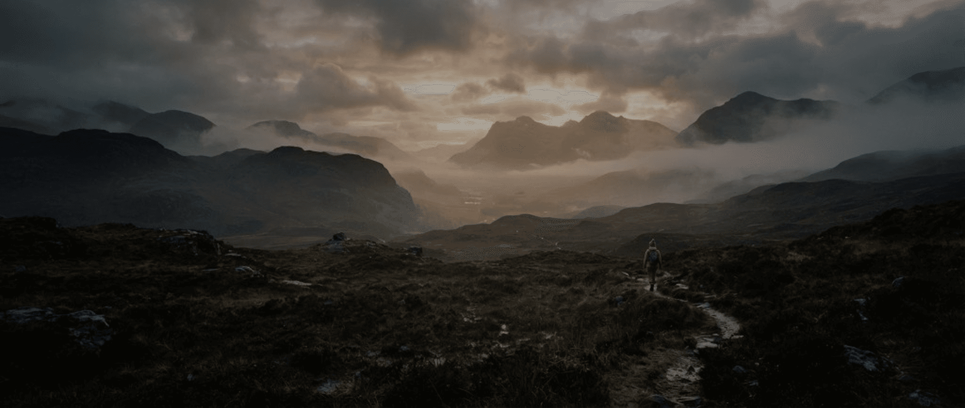 Hiker on a mountain path through a misty highland valley