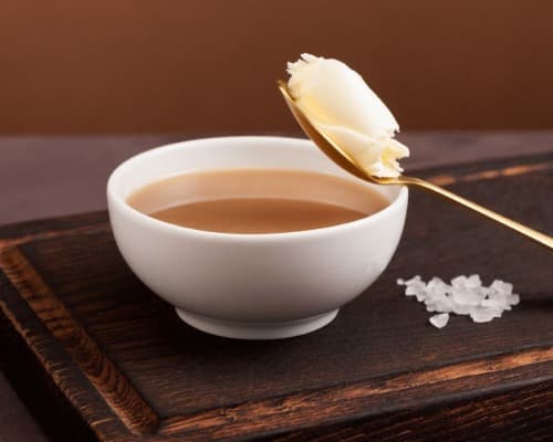 Ceramic bowl with spoon and salt on wood